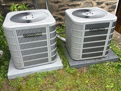 Two Concord air conditioning units on concrete pads, in a grassy area.