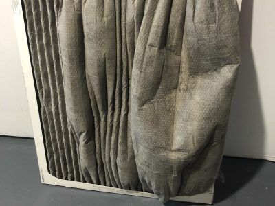 Used furnace filter, gray, pleated, in a white cardboard frame.