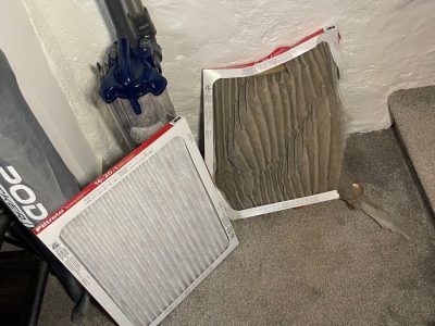 Two dirty air filters on the floor next to a vacuum cleaner and stairs.