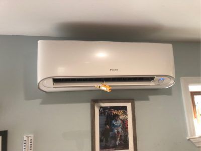 White wall-mounted air conditioning unit above a framed picture on a gray wall.
