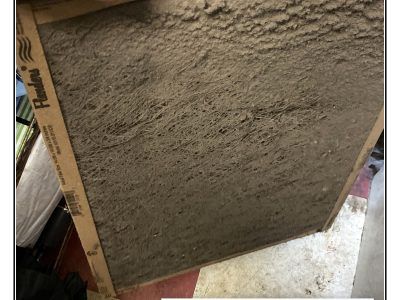 A very dirty air filter, covered in a thick layer of dust and debris, sitting on a floor.