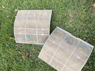 Two rectangular air filters covered in dirt, lying on green grass.