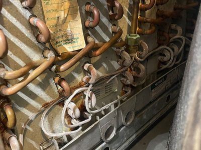 Close-up of an HVAC unit's copper tubing and wiring, showing signs of corrosion and age.