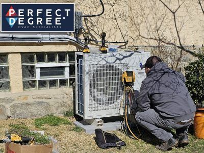 HVAC technician working on an outdoor air conditioning unit next to a building.