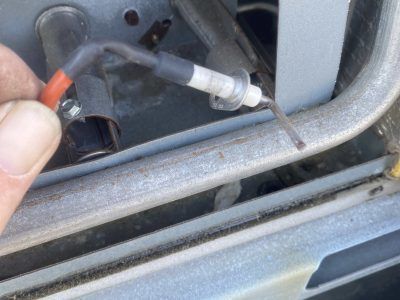 Hand holding a gas furnace igniter probe with a wire, near a metal tube.