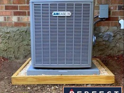 AirEase air conditioning unit on a wooden and gravel base, against a brick wall.
