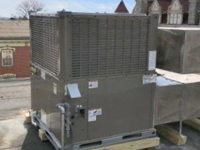 Rooftop HVAC unit, gray metal, on wooden pallets, with large grille. Adjacent building in background.