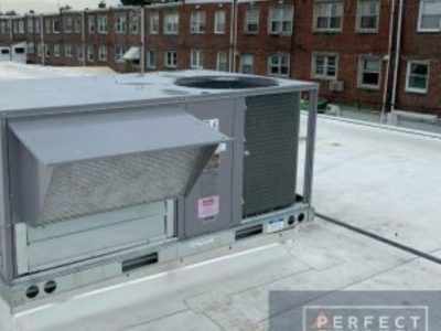 HVAC unit on a flat roof, partially covered in snow, with a brick building in the background.