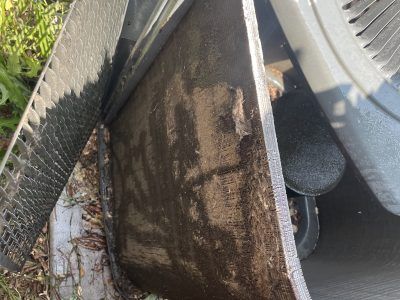 Close-up of a damaged, wet, black industrial component, possibly part of machinery or a vehicle, outdoors.