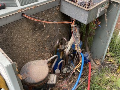 AC unit components, including a compressor, wiring, and refrigerant lines, exposed and dirty, in an outdoor setting.