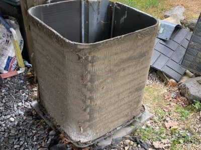 Dirty, square air conditioner unit outdoors, covered in dust and debris.