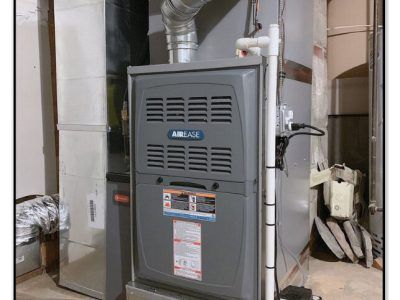 Gray furnace in a basement setting with ductwork and piping.