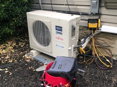 Fujitsu heat pump unit outside a building, with gauges attached, and a service bag nearby.