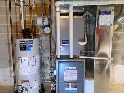 Water heater and furnace with connected pipes in a basement setting.