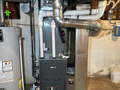 Furnace and water heater in a basement with ductwork and pipes visible.
