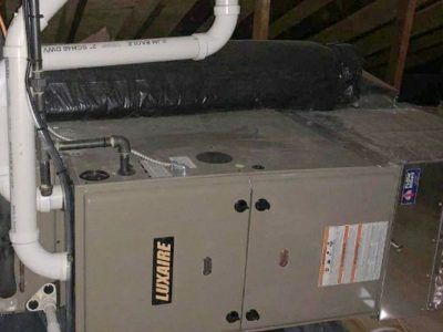 Luxaire furnace in an attic with white PVC pipes and a black insulated duct.