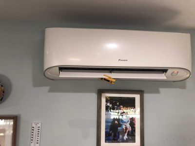 White air conditioner unit mounted on a light blue wall, above a framed photo.