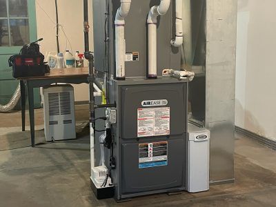 Furnace system in a basement. The unit is gray and white, with PVC pipes and a white humidifier.