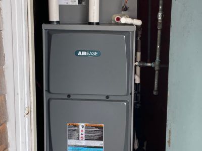 A gray AirEase furnace unit installed in a utility closet with white pipes and a gas line.