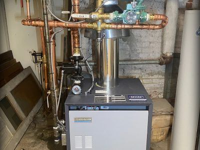 A modern boiler in a basement, with copper pipes and a pump.