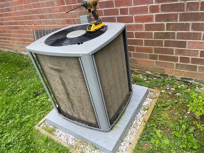 Air conditioning unit with a power drill on top, dirty screen, near a brick wall and grass.