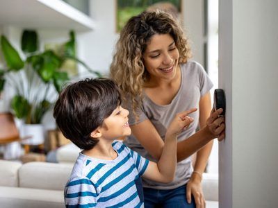 Woman and child looking at a smart home device on a wall, smiling. Indoors, bright room.