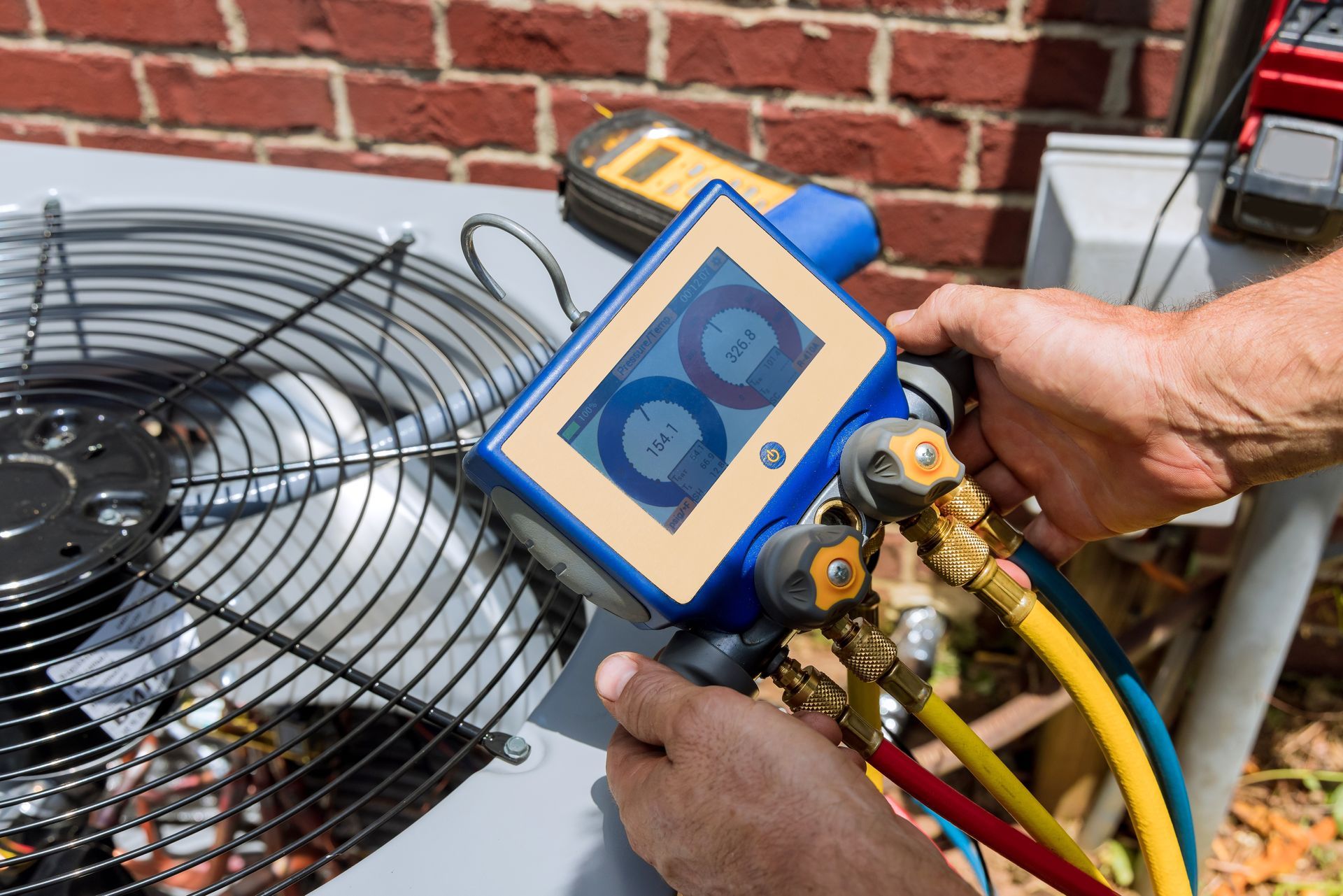 A technician holds a digital manifold gauge connected to an outdoor HVAC unit, checking refrigerant pressures.