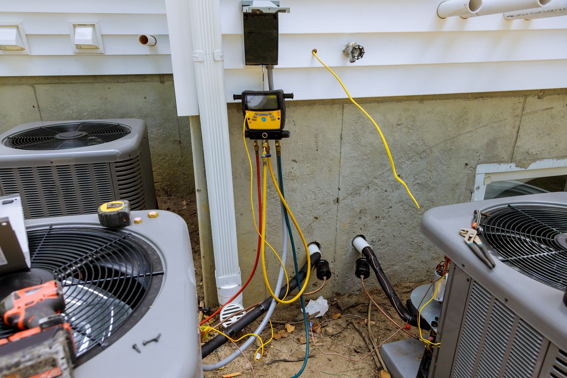 Digital gauges connected to air conditioning units with hoses, indicating an ongoing HVAC repair or maintenance service.