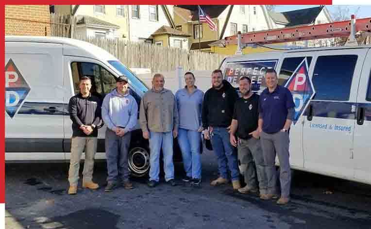 Group of men standing in front of two company vans with a US flag in the background.
