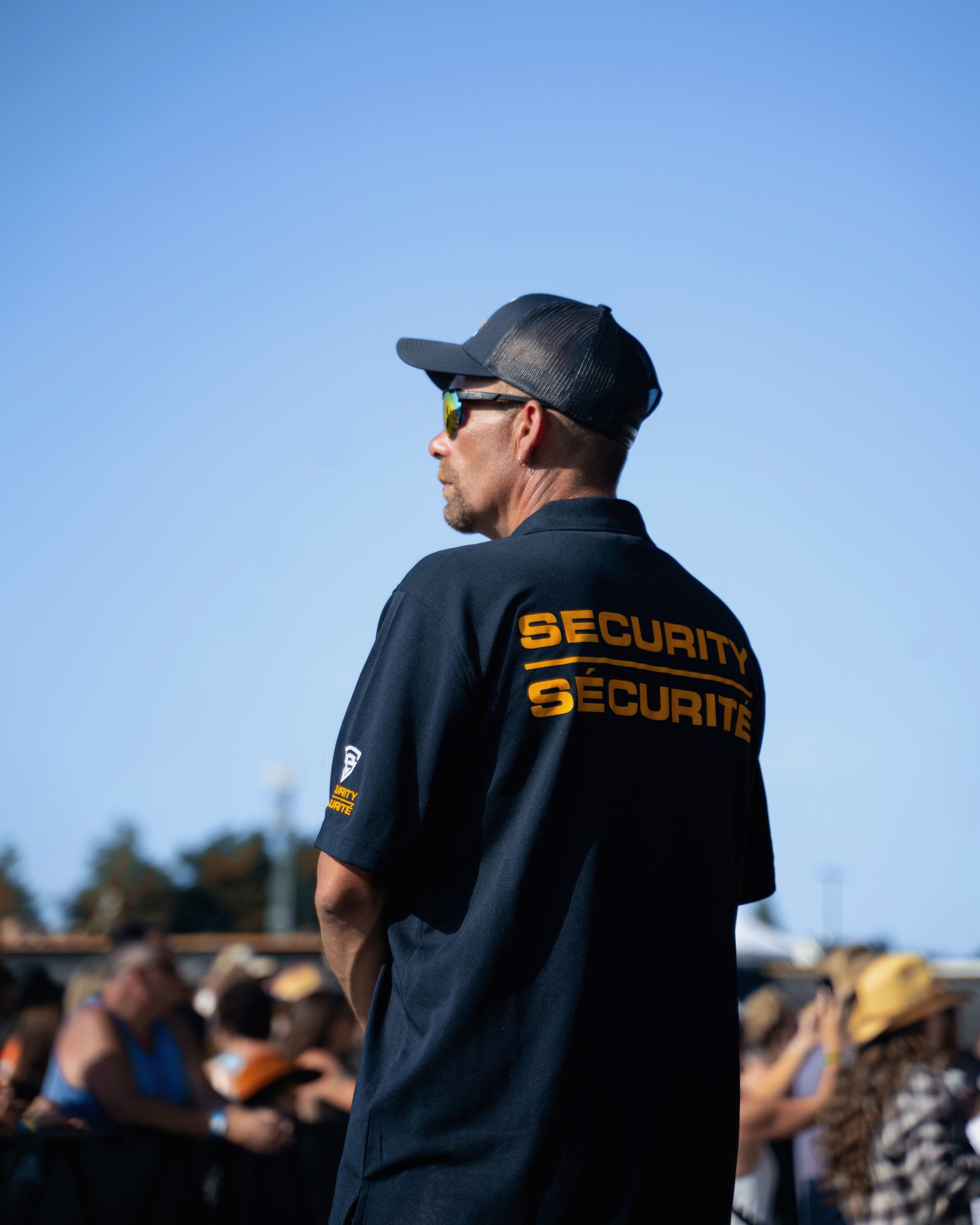 A man wearing a security shirt is standing in front of a crowd.