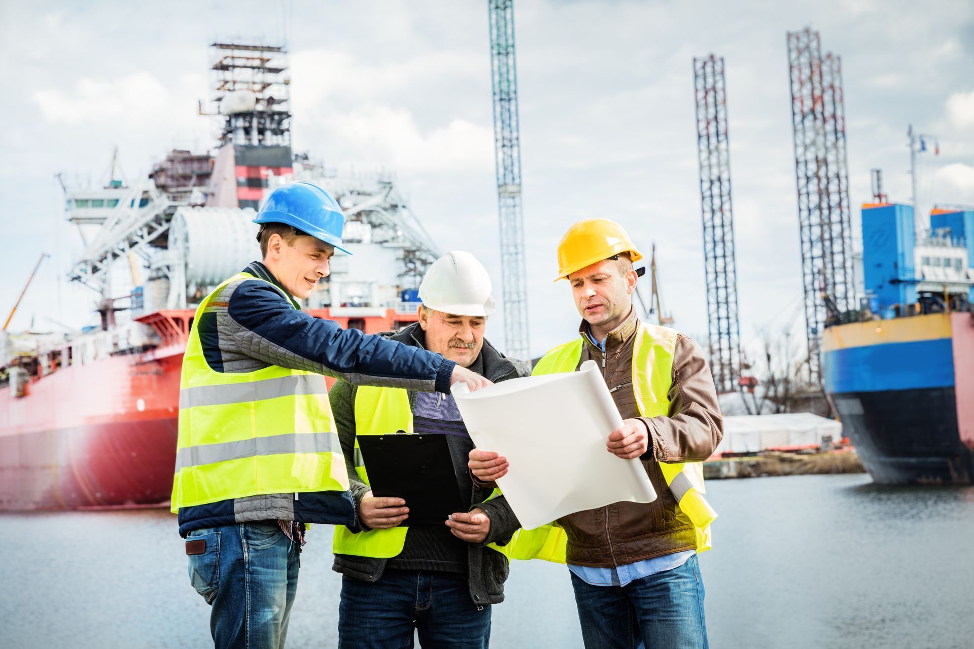 three construction workers are looking at a blueprint in a harbor .