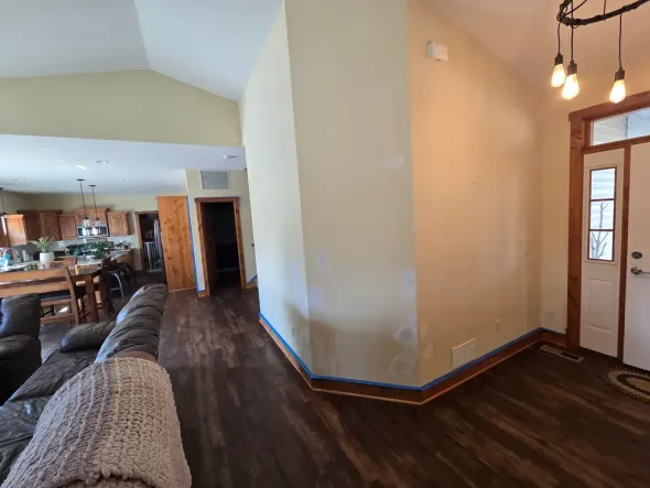 Living room with wood floors, beige walls, brown trim, and a view into the kitchen.