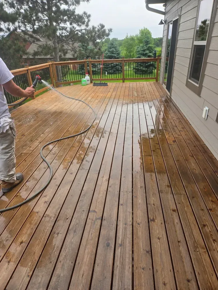 Person washes a wet wooden deck with a hose.