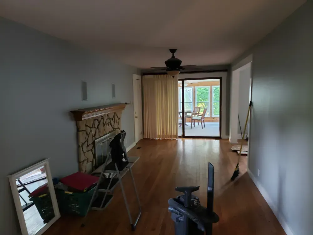 Empty living room with fireplace, hardwood floors, and sliding glass door to a sunroom.