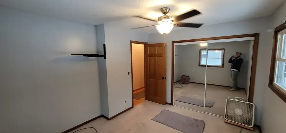 Bedroom with a ceiling fan, mirrored closet doors, and a person reflected inside.