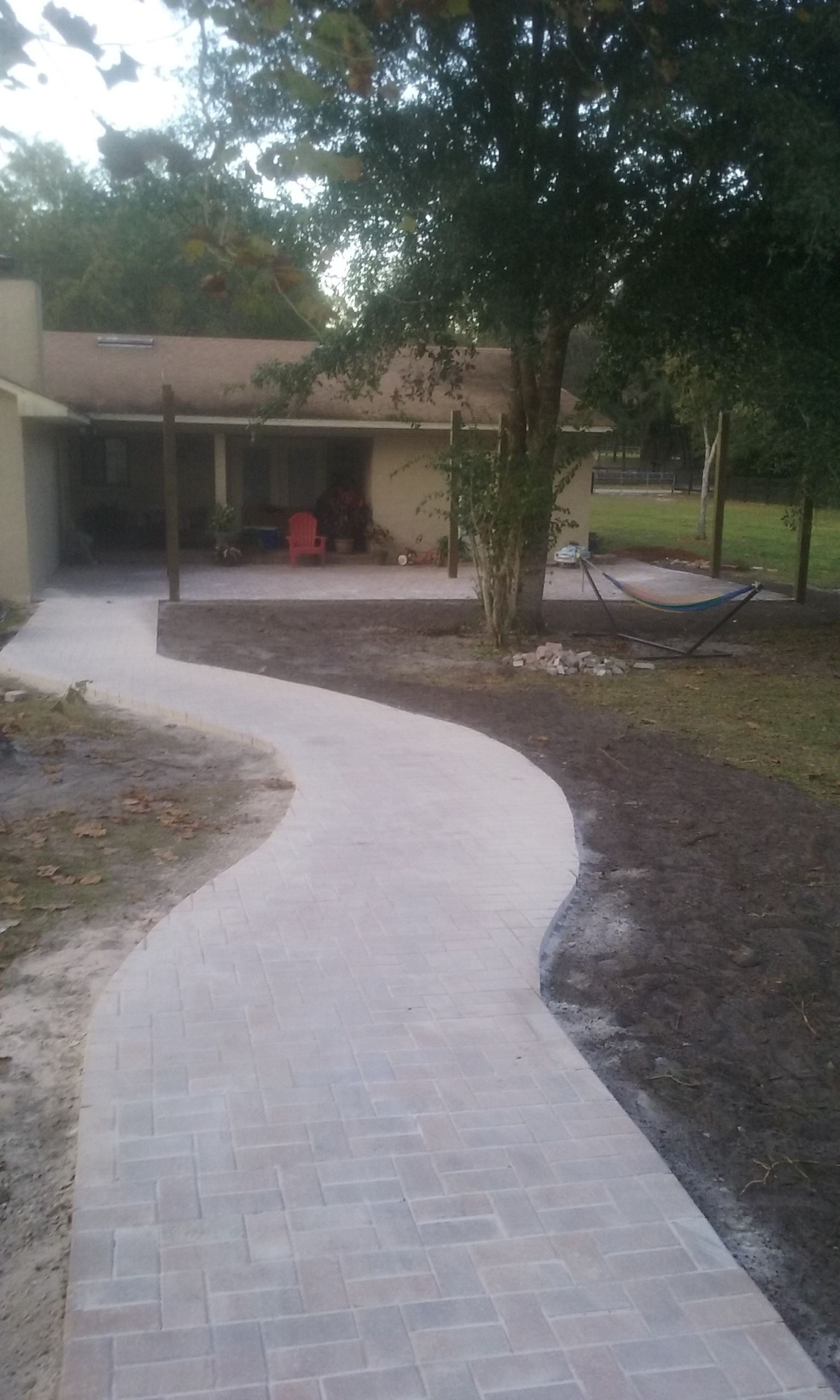 A concrete walkway leading to a house with trees in the background.
