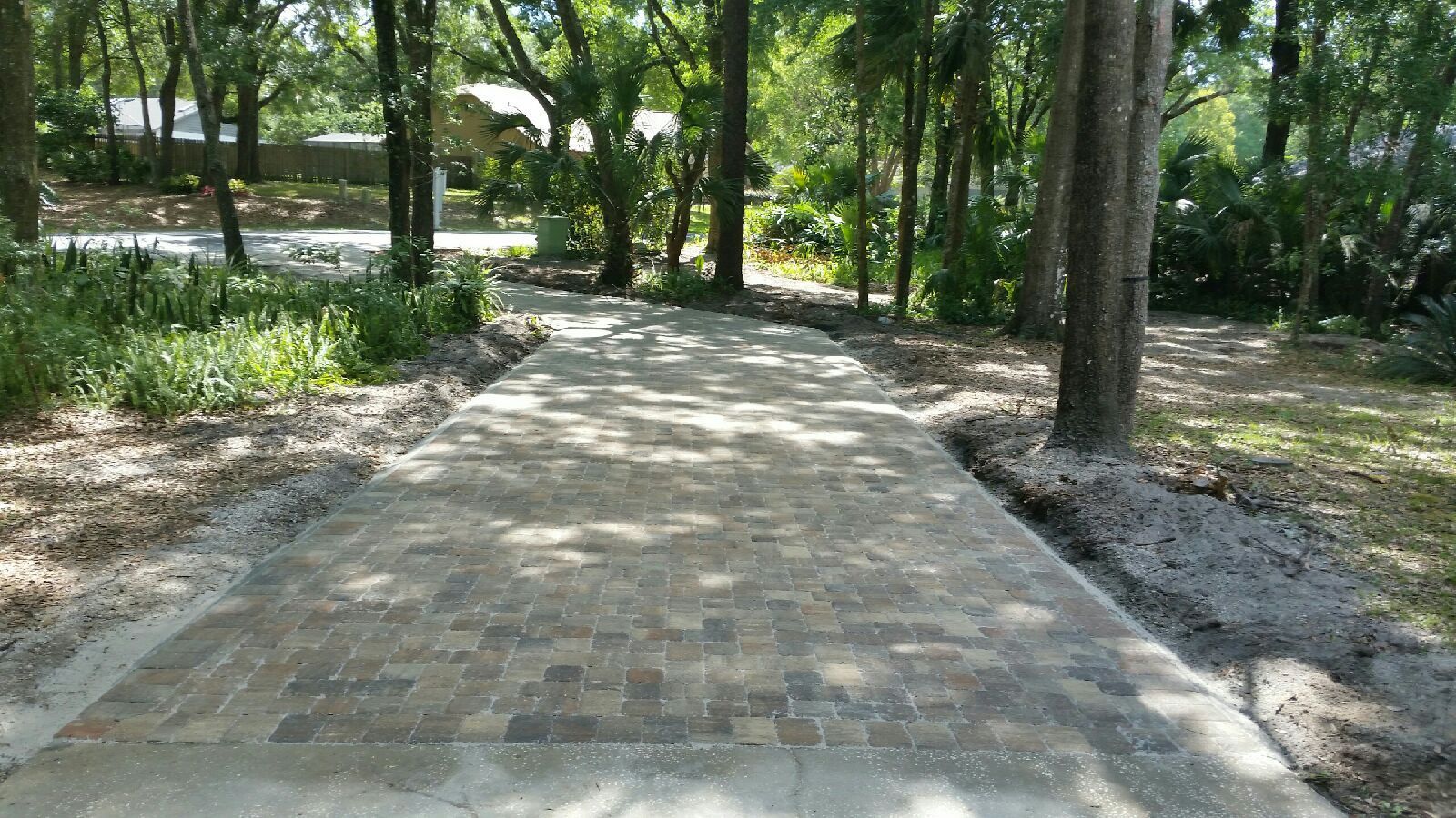 A brick driveway leading to a house in the woods.