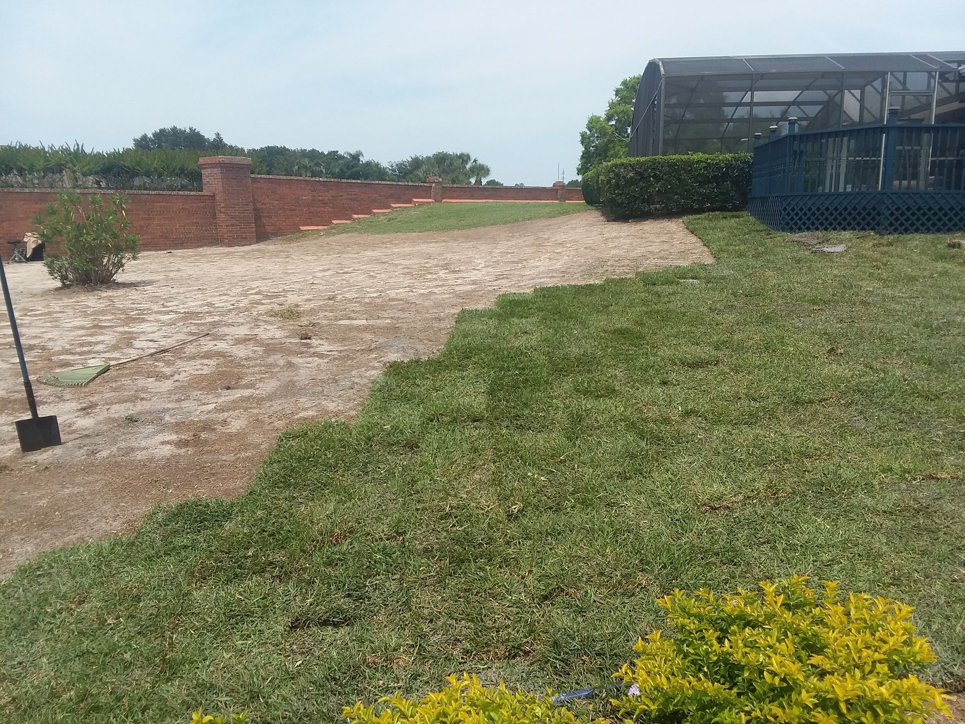 A shovel is sitting in the grass next to a brick wall.