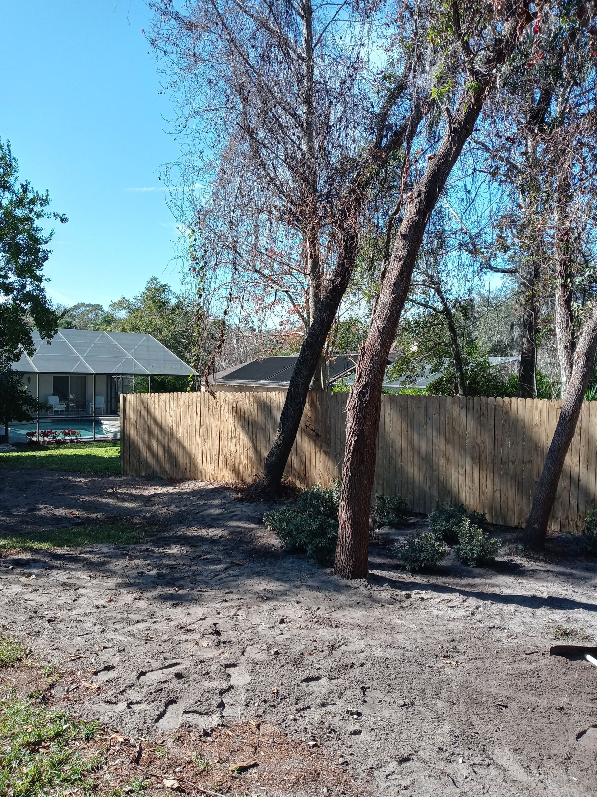 A wooden fence is surrounded by trees and dirt in front of a house.