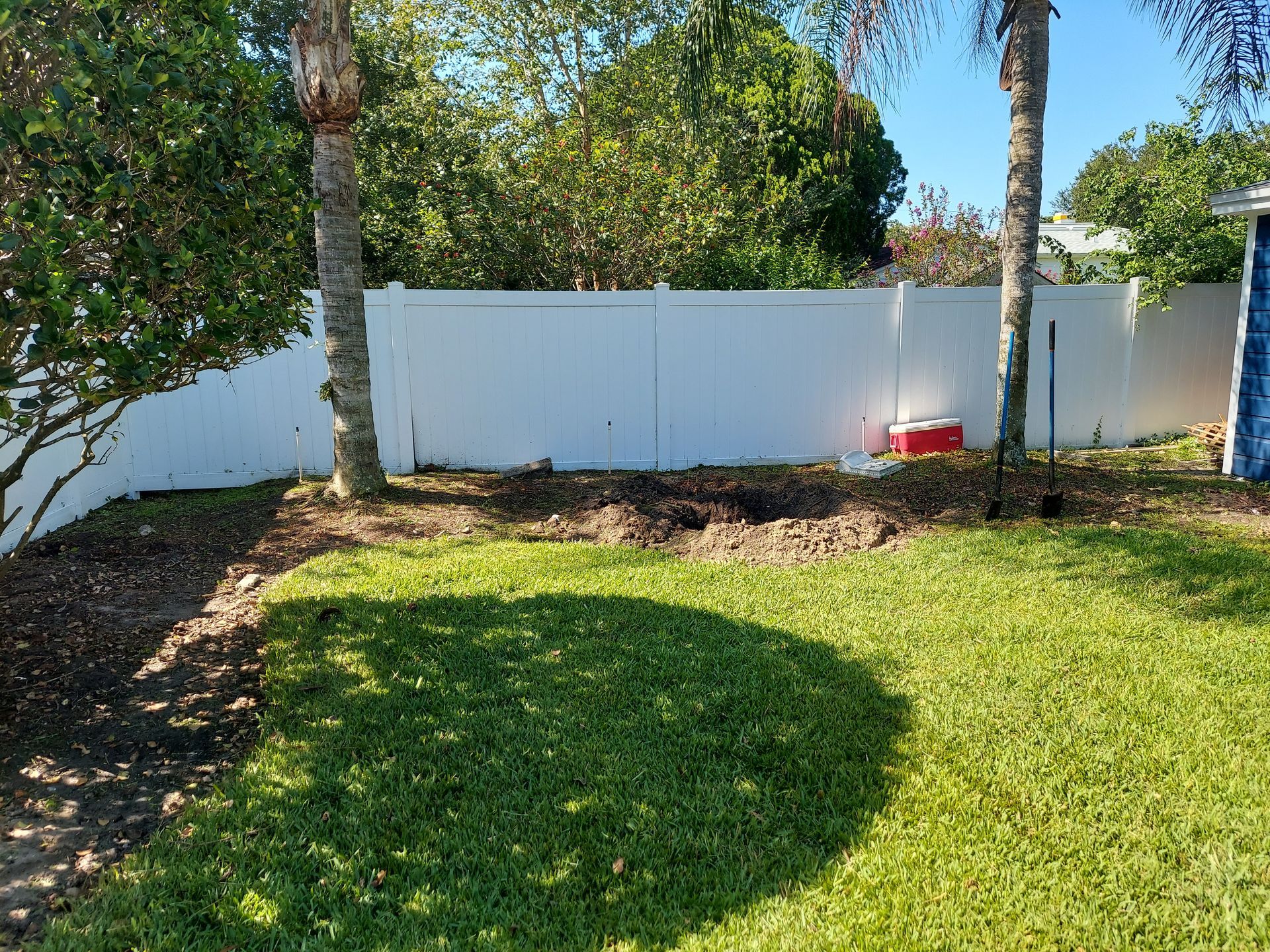 A backyard with a white fence and a red cooler.