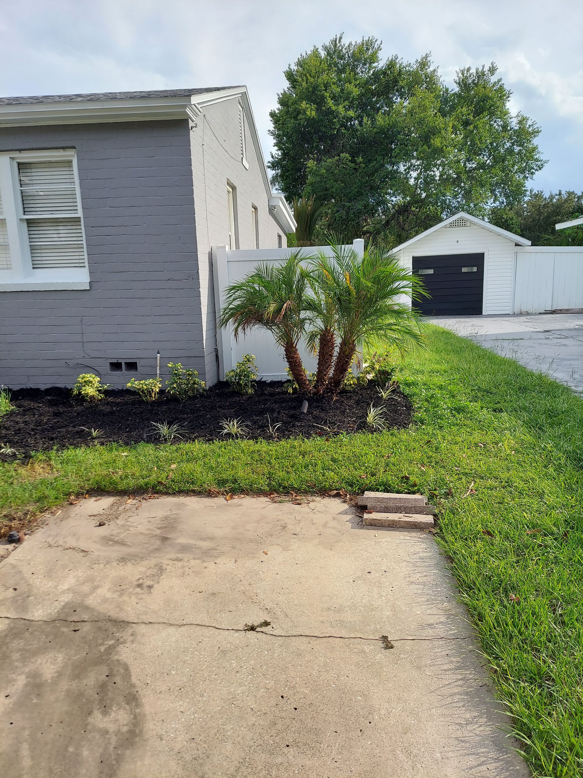 A gray brick house with a white fence and a black garage door.