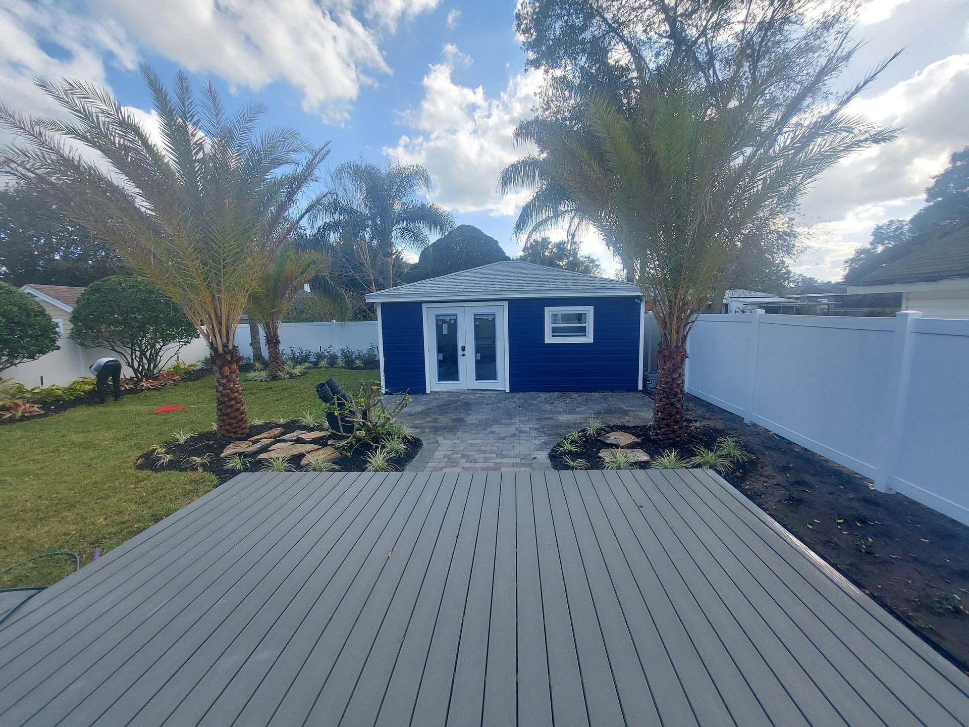 A blue house with a white fence and palm trees in front of it