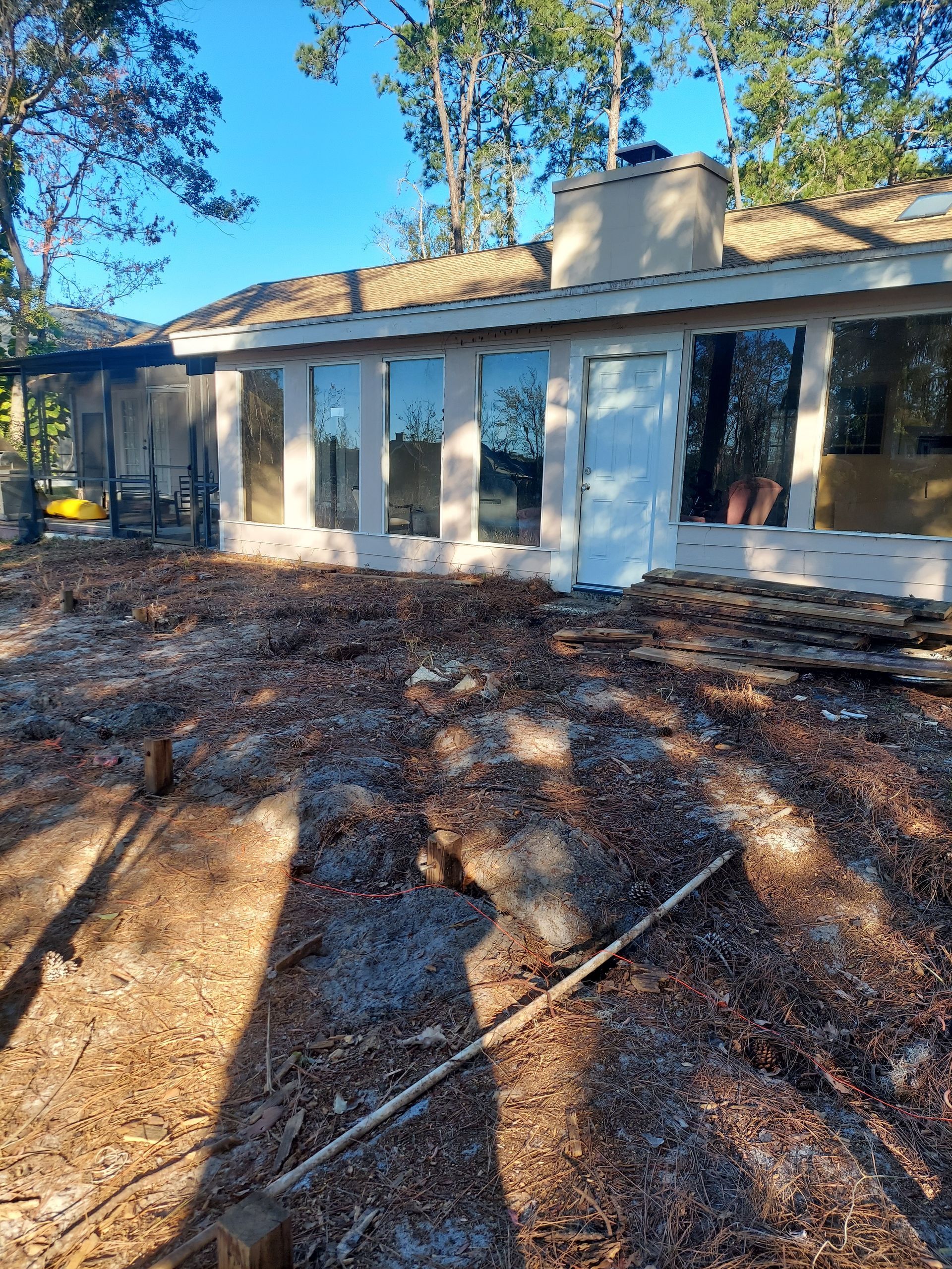 A white house with a lot of windows is sitting on top of a dirt field.