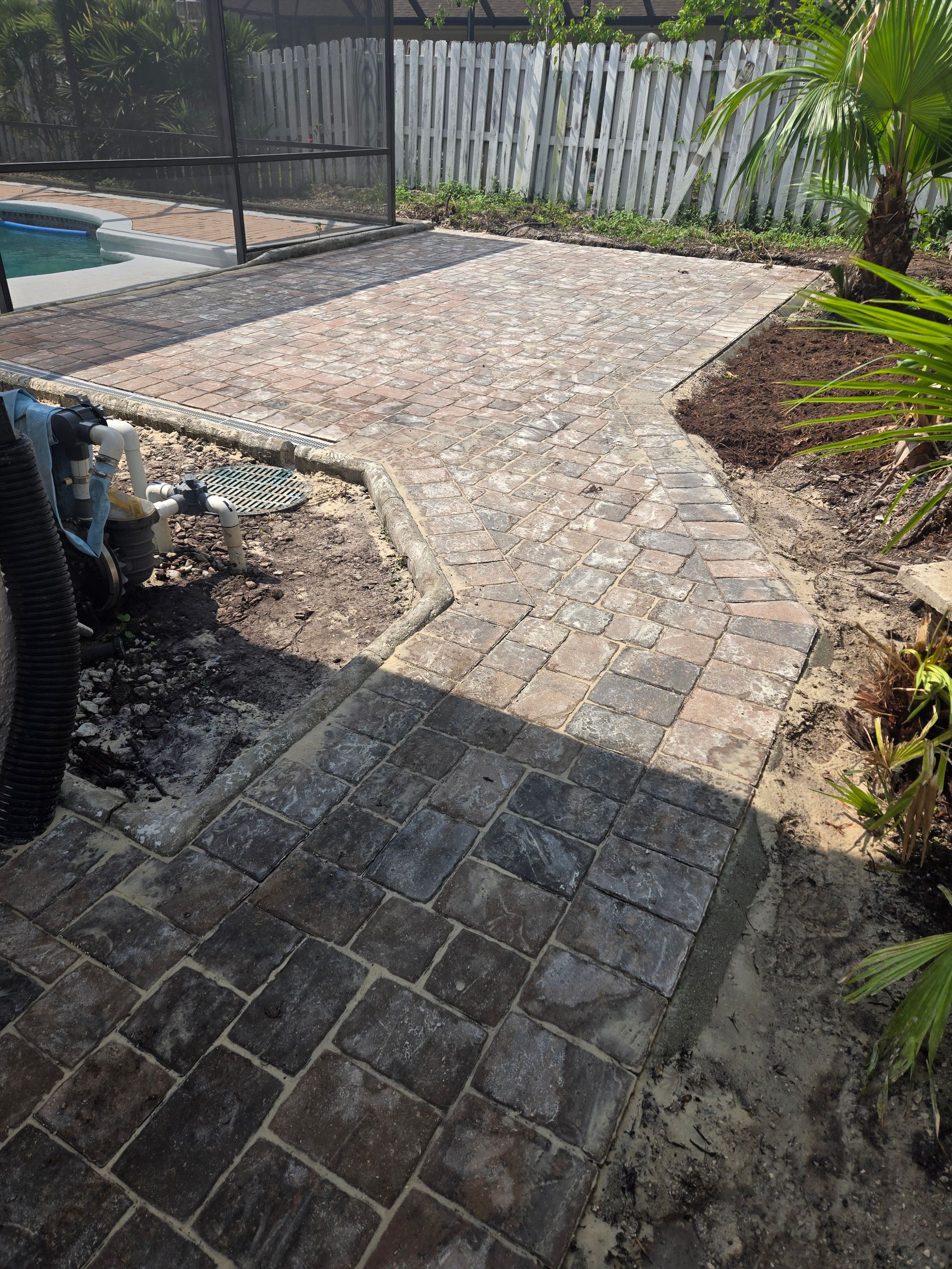 A brick walkway leading to a pool in a backyard.