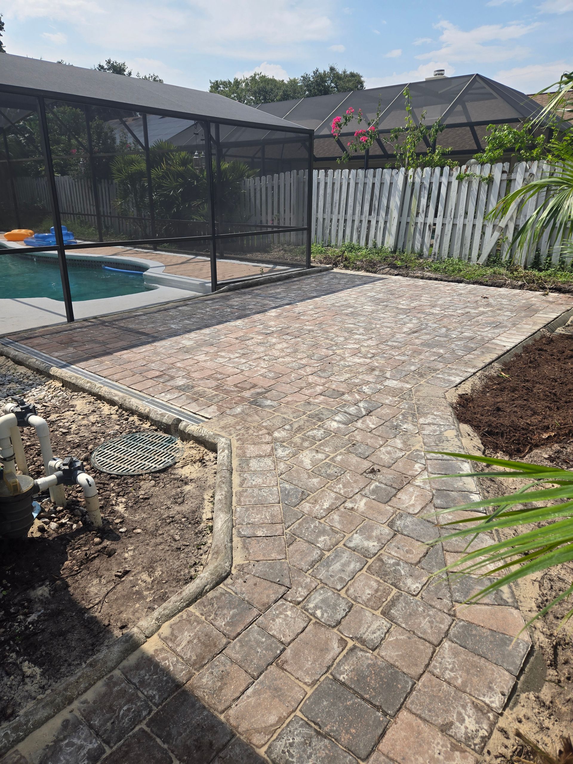 A brick walkway leading to a swimming pool in a backyard.