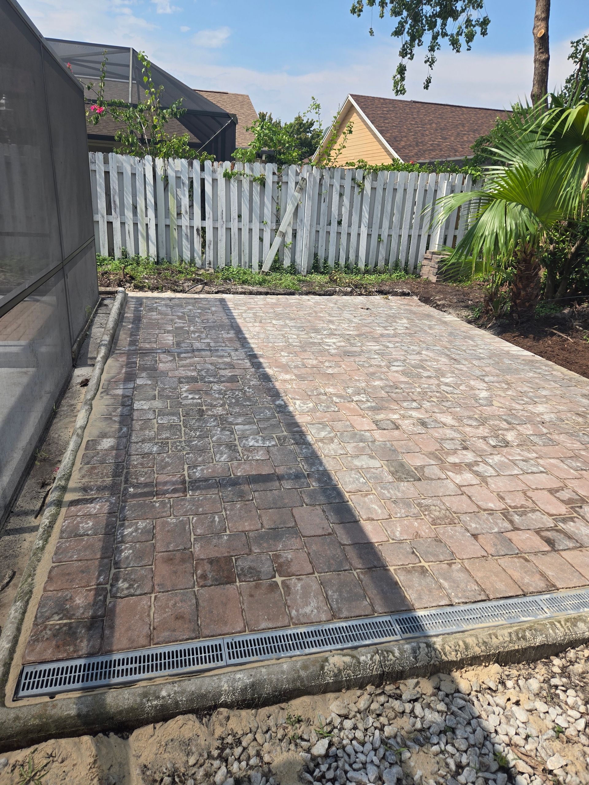 A brick walkway leading to a house with a white fence in the background.