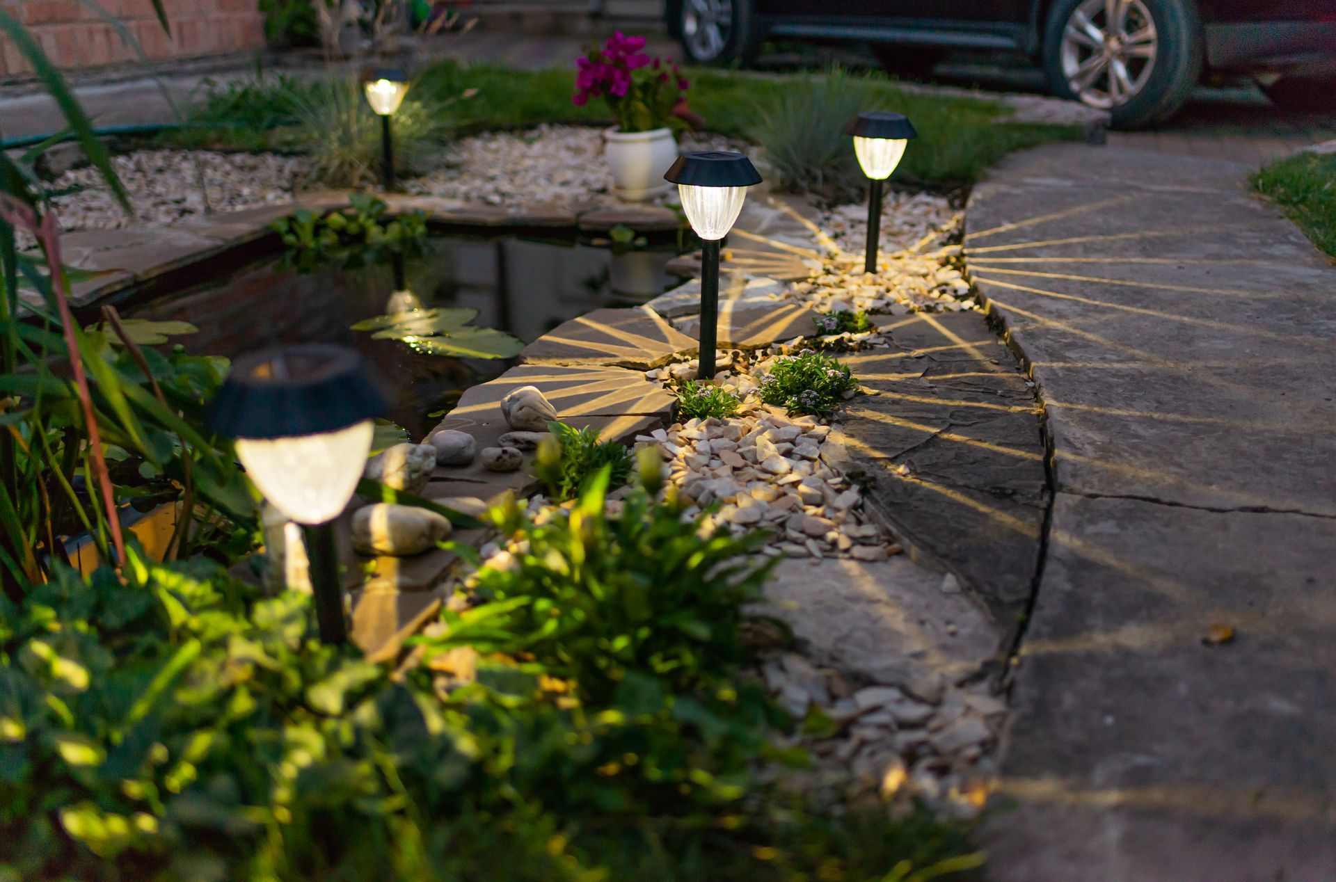 A car is parked in a driveway next to a pond with solar lights.