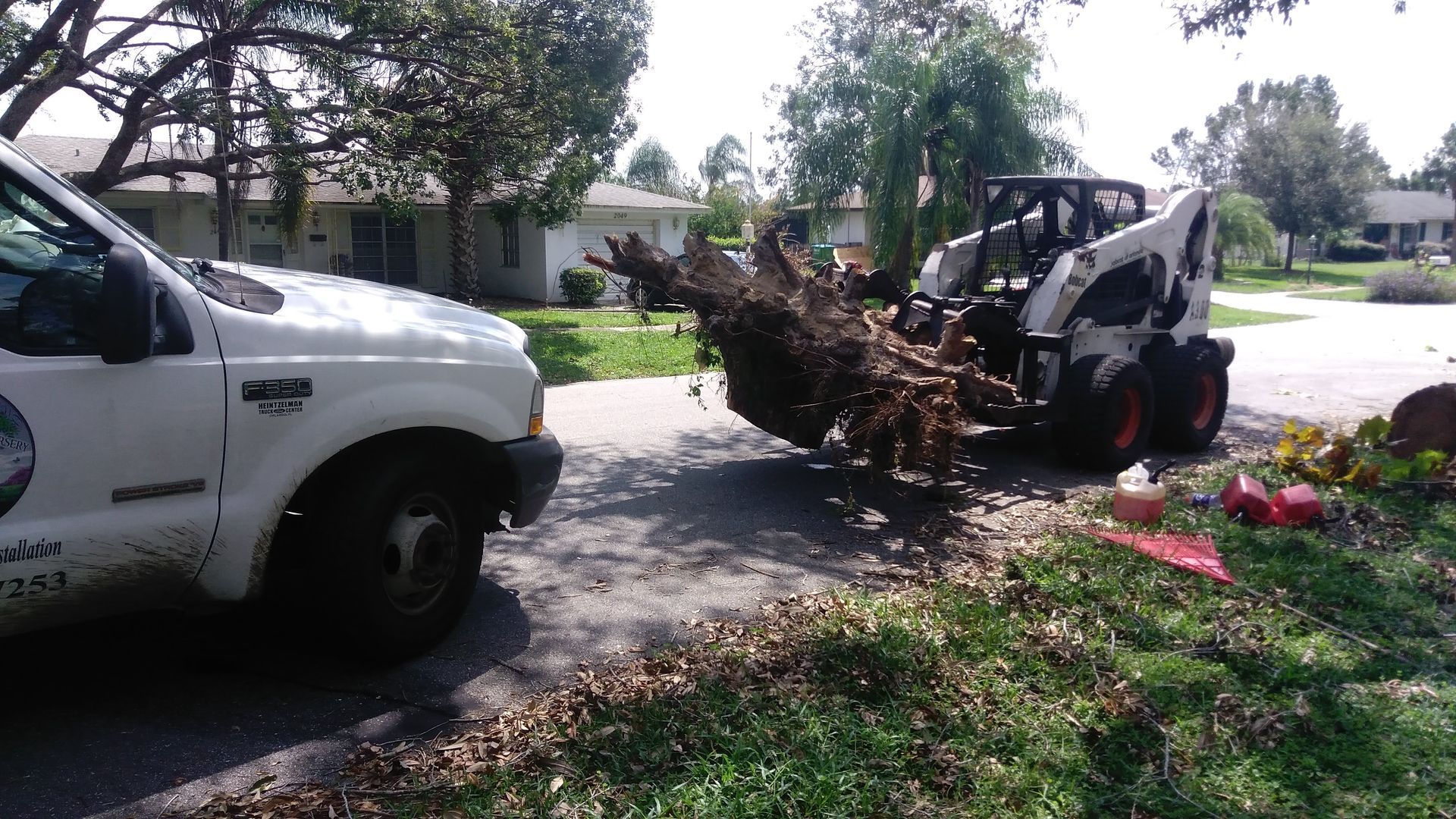 A white truck is parked next to a bulldozer carrying a large tree stump.