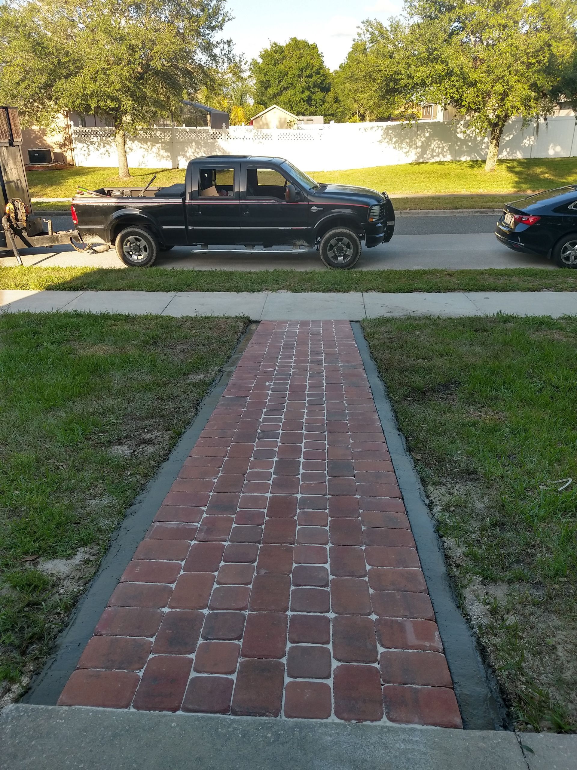 A black truck is parked on the side of the road next to a brick walkway.