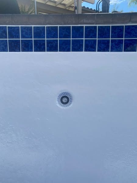 A white swimming pool with blue tiles and a drain hole in the middle.